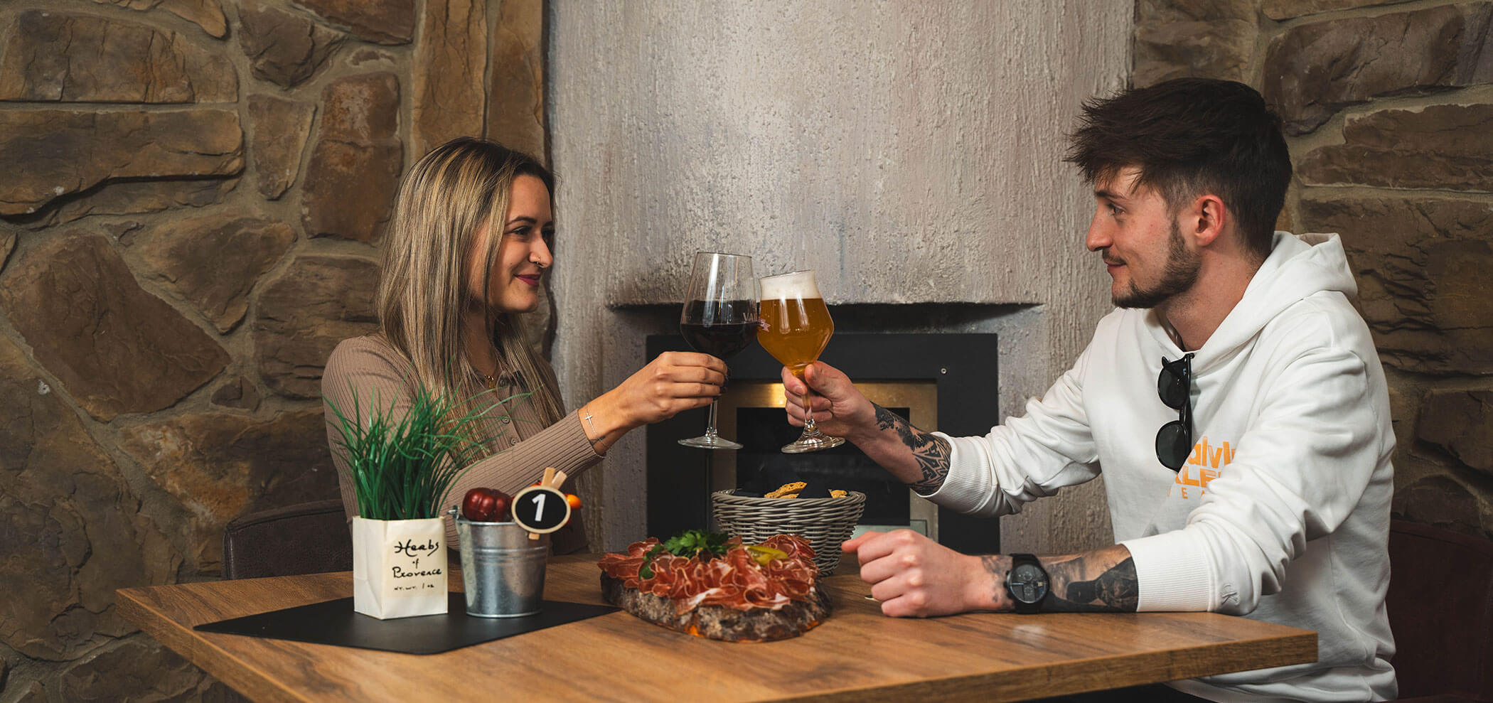 Ein Paar stoßt mit einem Bier und einem Rotwein im Senfter's Bistro an - Metzgerei Senfter