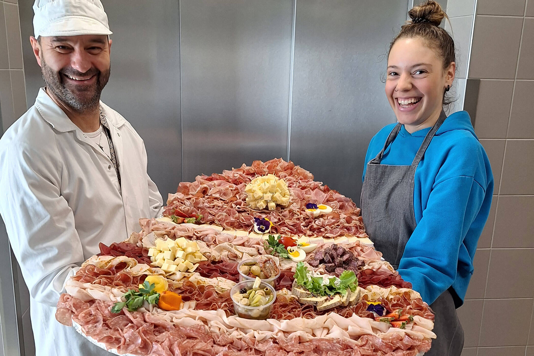 Zwei Mitarbeiter halten eine große Platte mit verschiedenen Wurstwaren und Käse in der Hand - Metzgerei Senfter